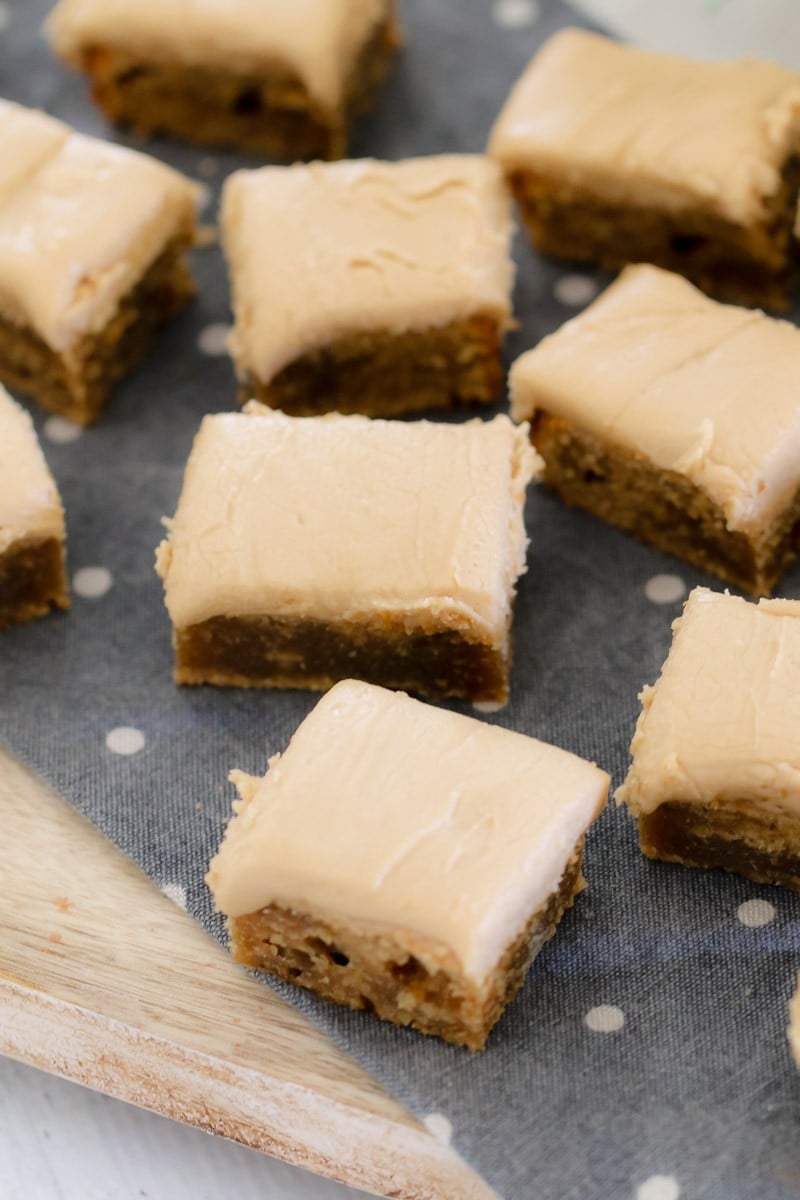 Looking down on squares of slice topped with caramel frosting on a blue tea towel