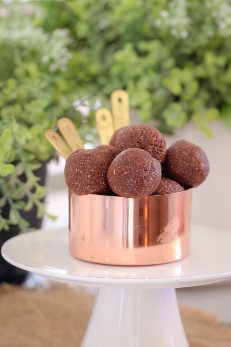 A copper measuring cup filled with chocolate bliss balls on a white stand