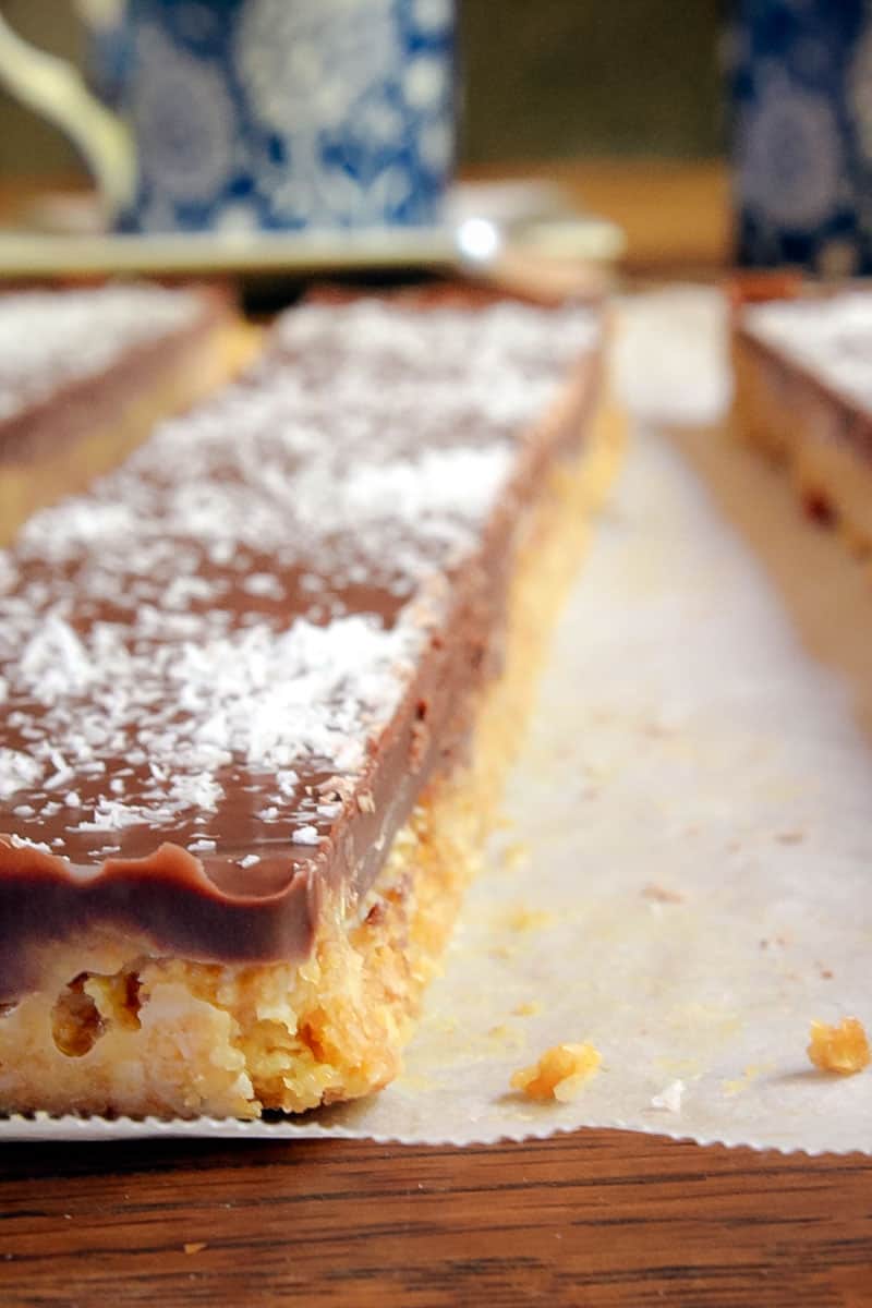 A close up of a cookie crumb slice with a chocolate topping and sprinkled with desiccated coconut.