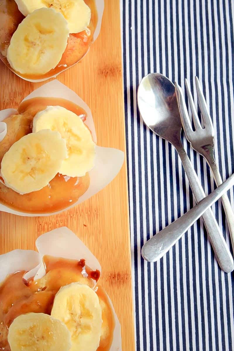 Muffins drizzled with caramel and topped with banana slices on a board next to a spoon and fork