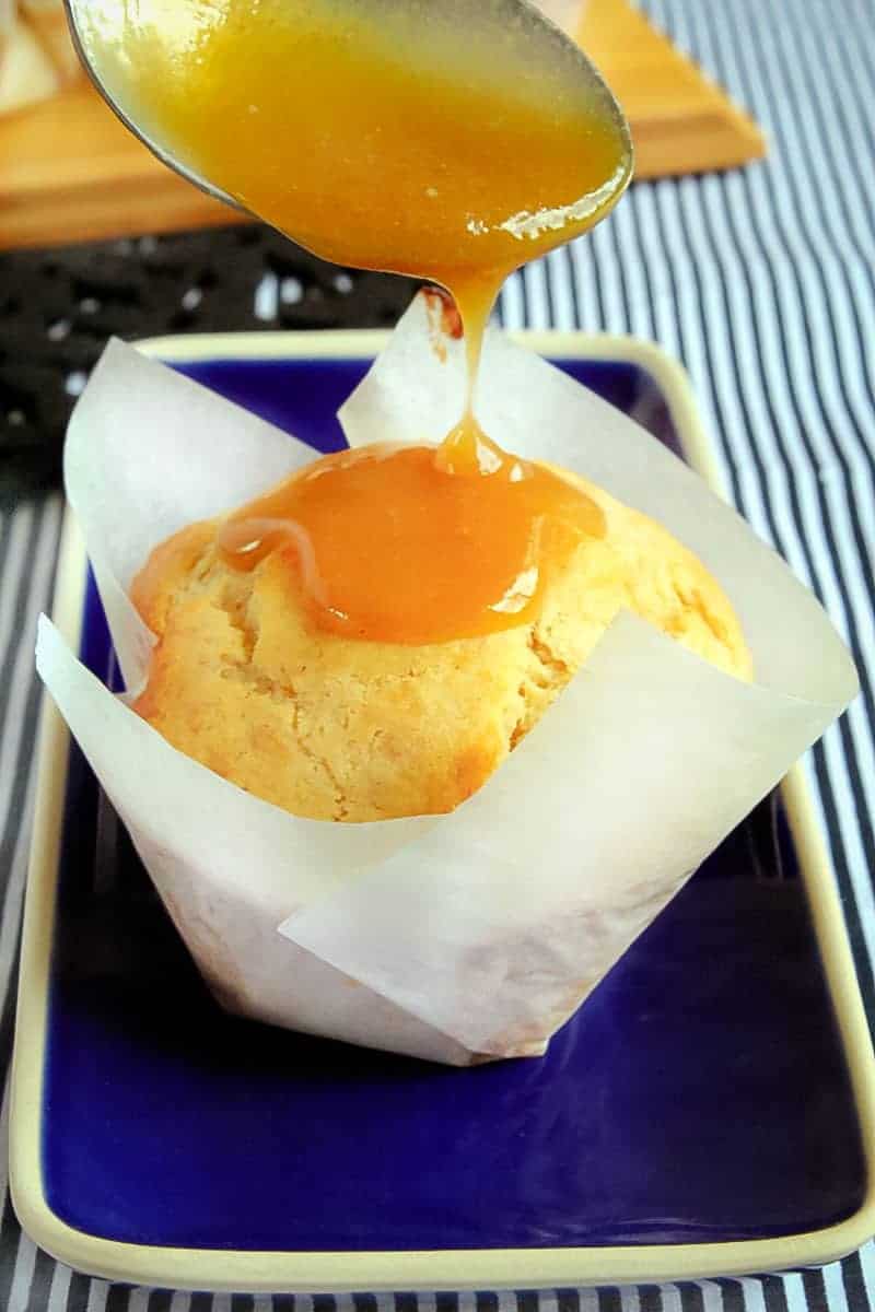 A muffin wrapped in baking paper, with caramel sauce being drizzled over it
