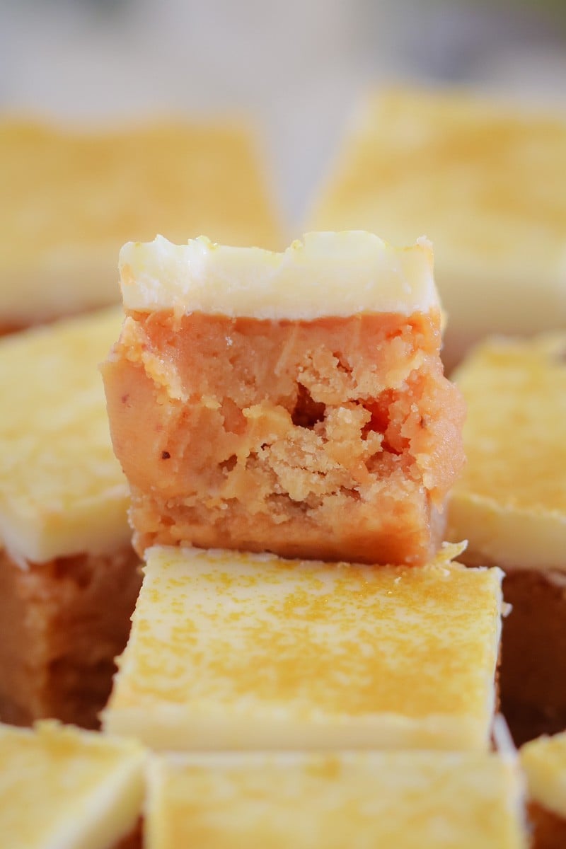 Squares of a buttery sweet slice topped with white chocolate, with one piece on top half eaten