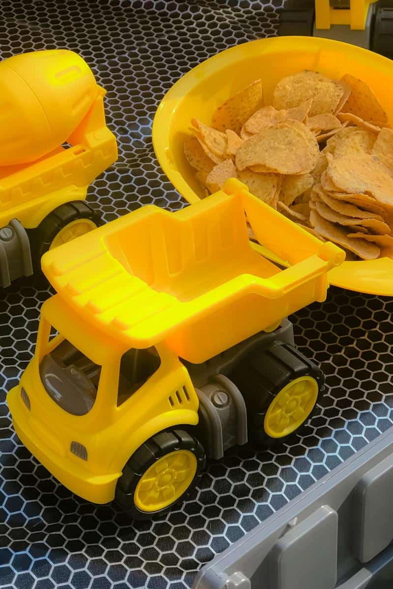 A yellow mini tip-truck in front of a bowl of crisps