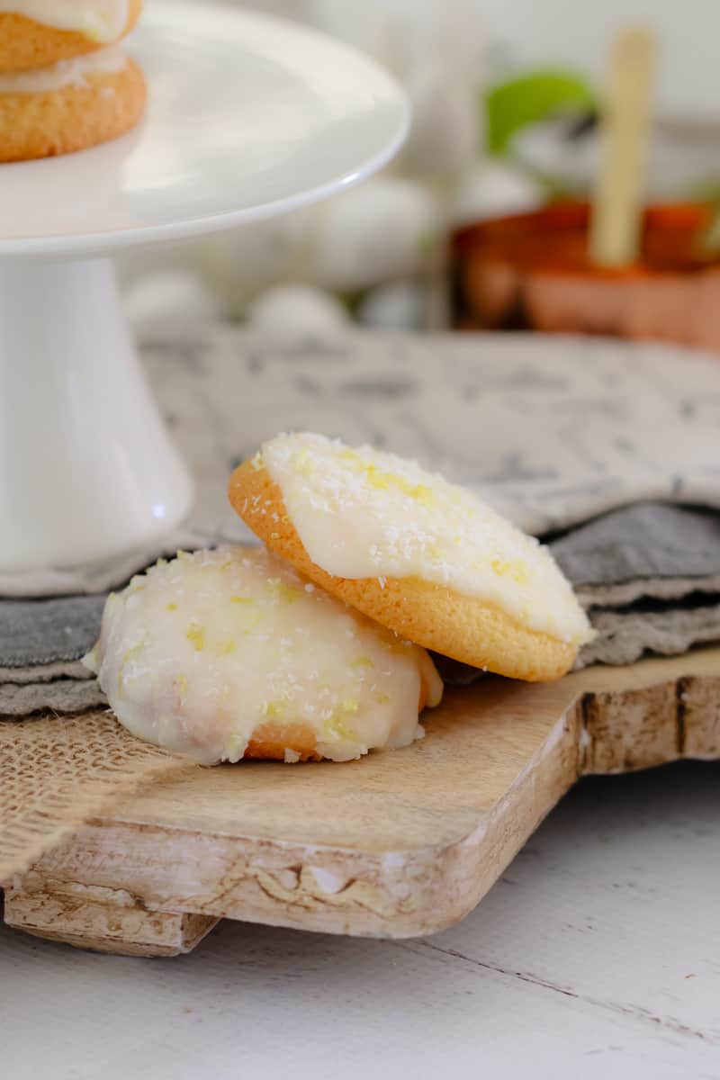 Two iced lemon coconut biscuits on a wooden board