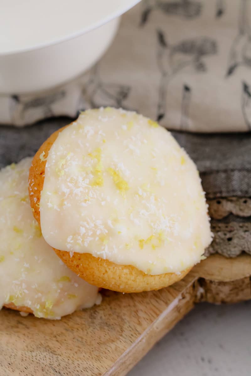 A close up of two iced lemon coconut biscuits on a wooden board