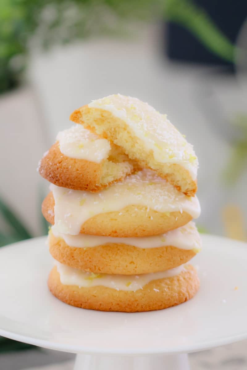 A close up of a stack of iced lemon coconut biscuits, with the top one broken in half