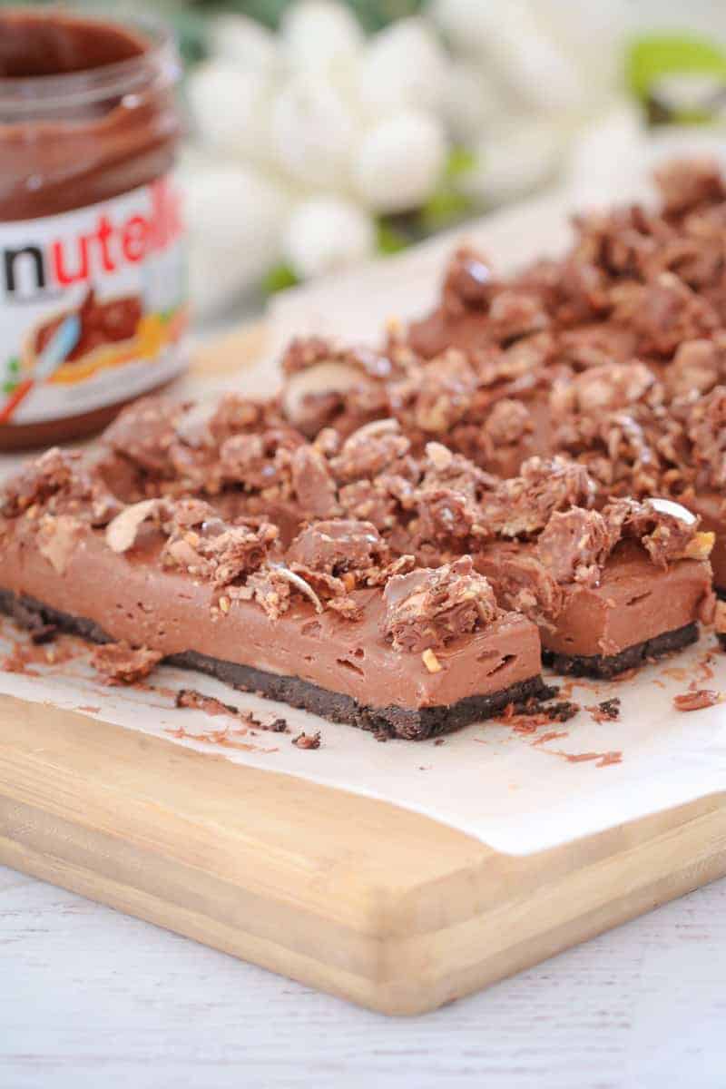 Pieces of a chocolate and cheesecake layered slice topped with crumbled chocolate on a wooden board