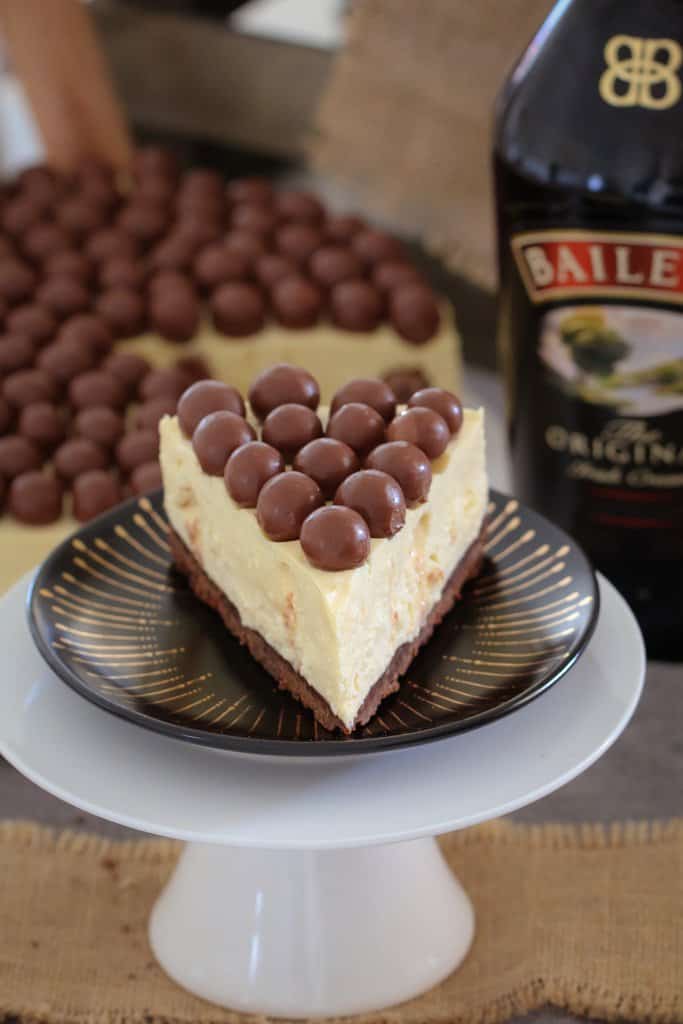 A plate with a serve of cheesecake decorated with Malteser lollies on top with a bottle of Baileys behind