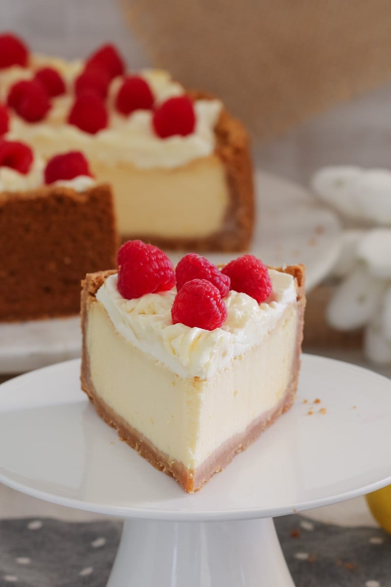 A slice of baked lemon cheesecake with cream and raspberries. 