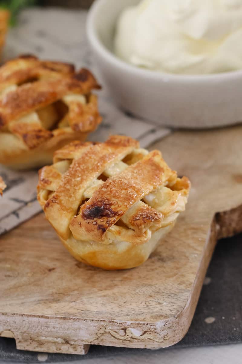 A close up of mini apple and caramel pies topped with pastry lattice served on a wooden board