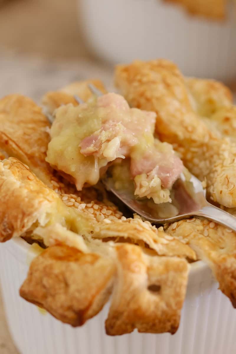 A close up of a forkful of chicken and leek pie with a pastry lattice topping in a ramekin