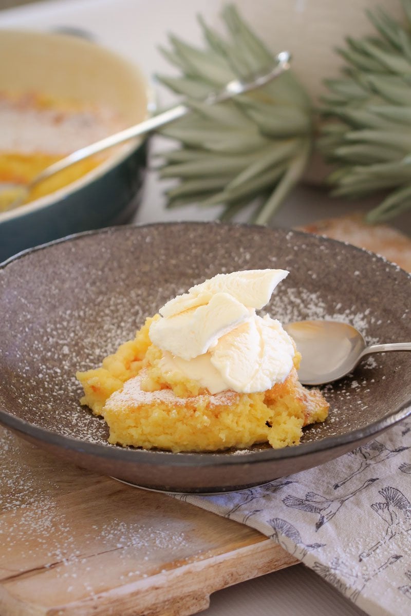 A grey bowl with a serve lemon delicious pudding topped with ice cream