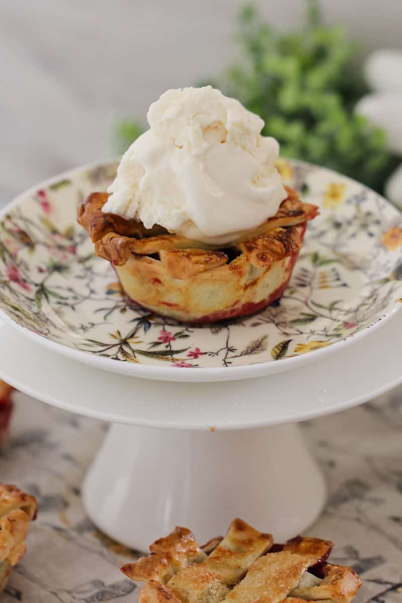 A close up of a mini berry pie topped with whipped cream served on a floral plate