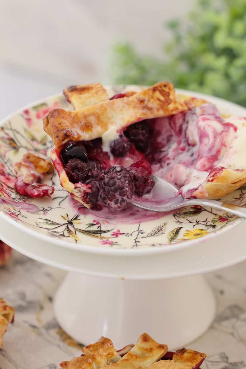 A floral plate and spoon with a mini berry pie half eaten to show a filling of berries
