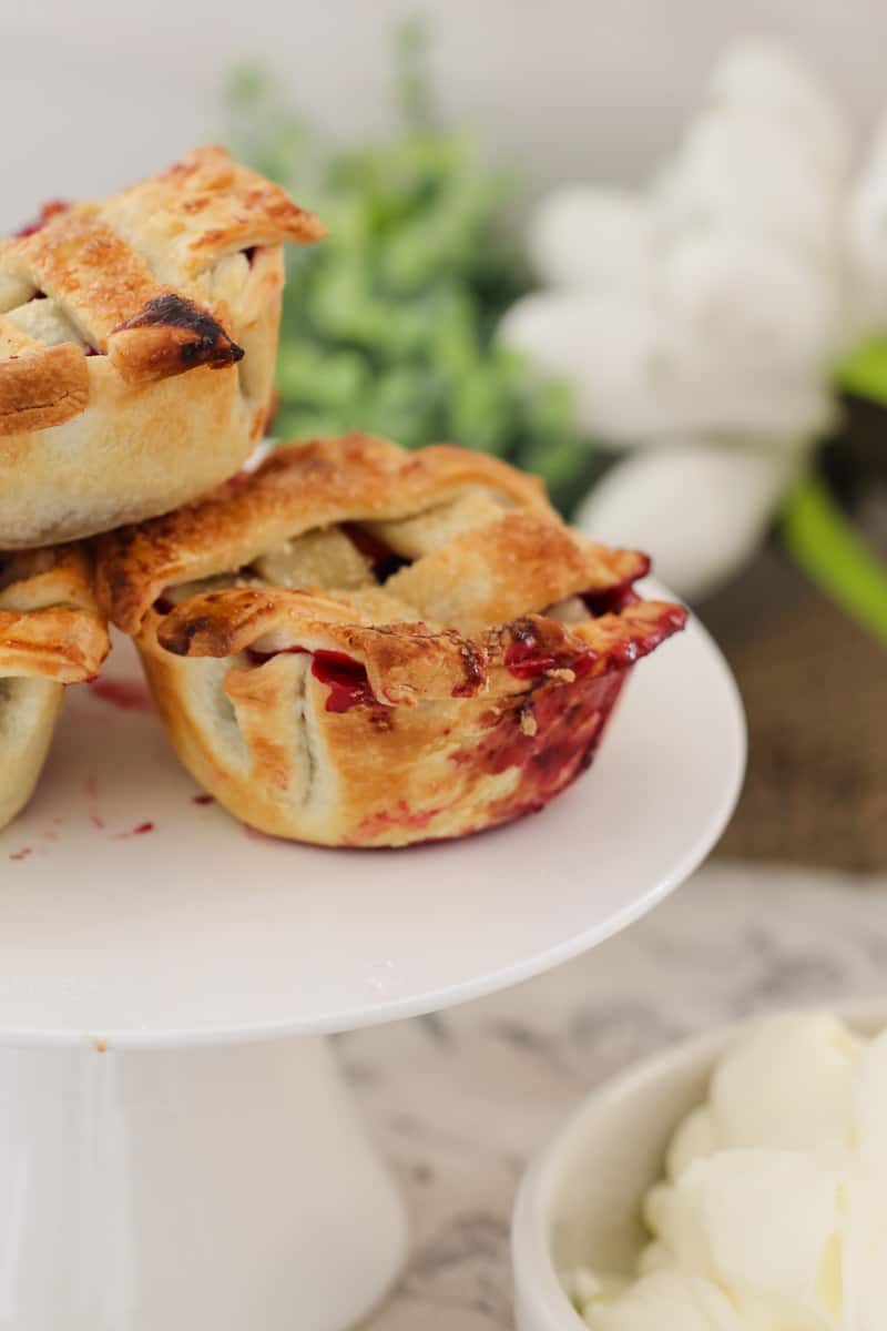 A close up of a stack of mini pies filled with mixed berries and topped with pastry lattice on a white cake stand
