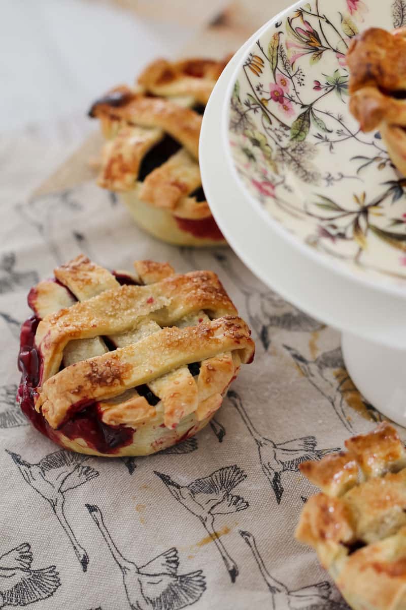 Mini pies filled with mixed berries and topped with pastry lattice on a tea towel