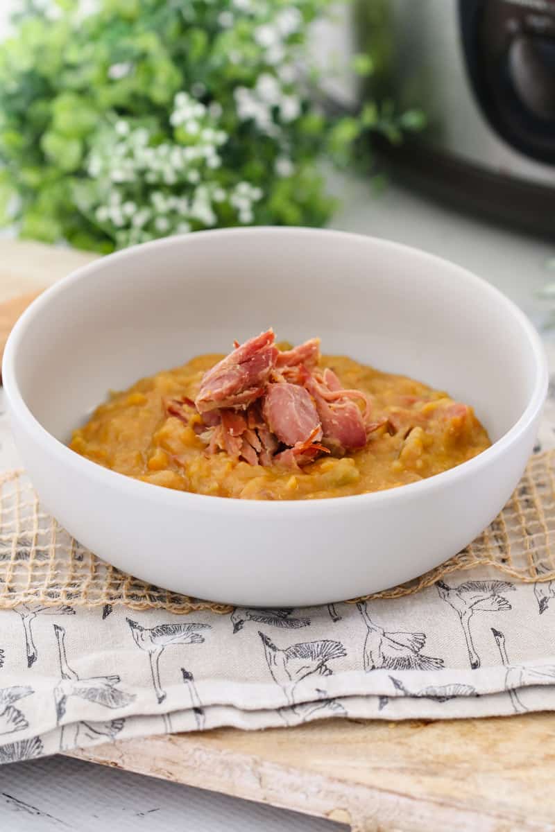 A white bowl filled with split pea soup with shredded ham on top.