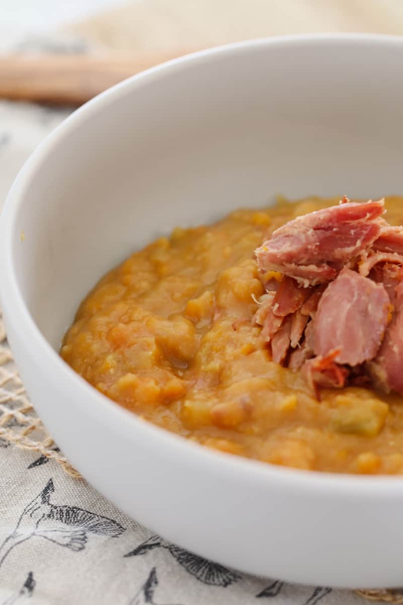 A white bowl filled with thick split pea soup and chunks of ham on top.