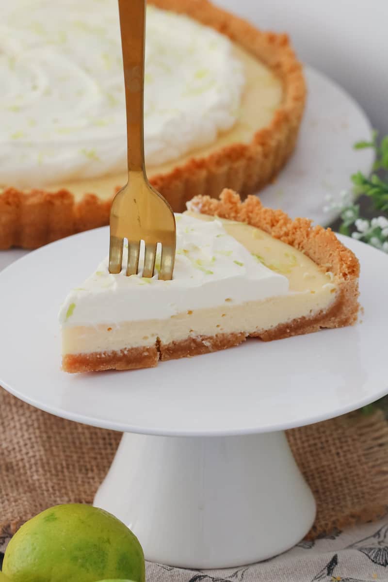 A serve of lime citrus pie with a fork standing up in it, on a white plate