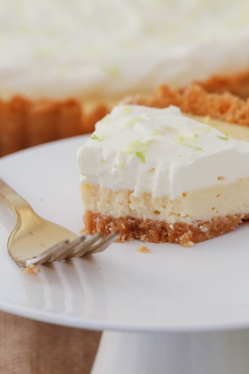 A half eaten piece of creamy layered key lime tart topped with whipped cream and lime zest.