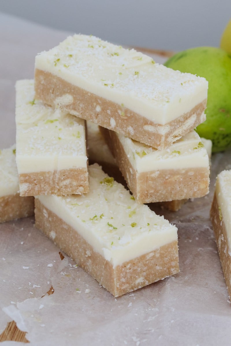 Pieces of a no-bake slice with white icing, stacked in front of a fresh lime