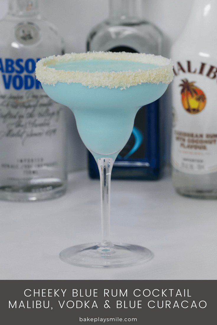 A cocktail glass with a sugared rim, filled with a blue cocktail in front of bottles of vodka and Malibu