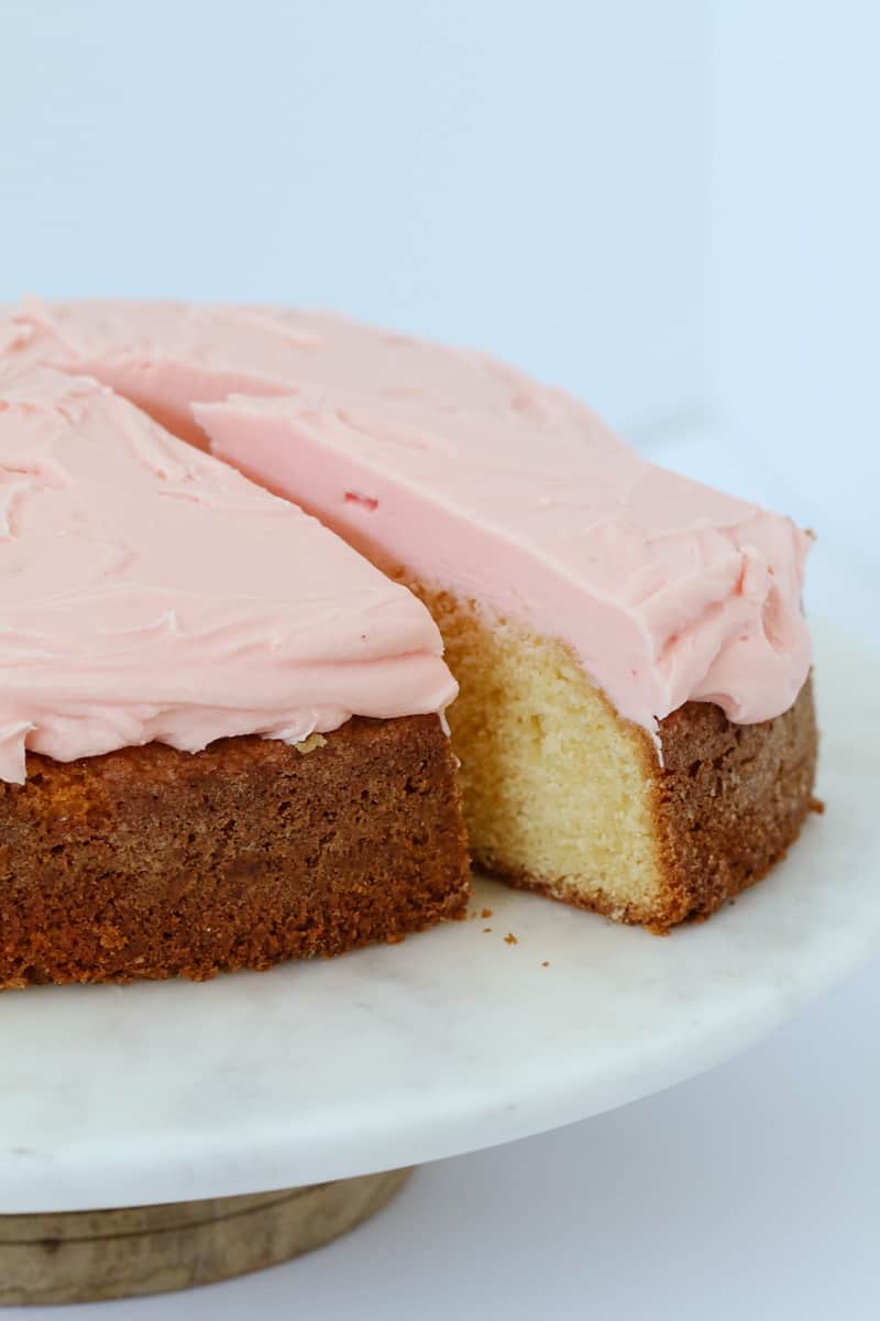 A slice of white cake with pink icing being removed from the entire cake.