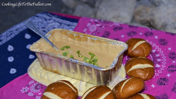 Beer cheese dip with spring onions in a foil container with bread around the outside. 