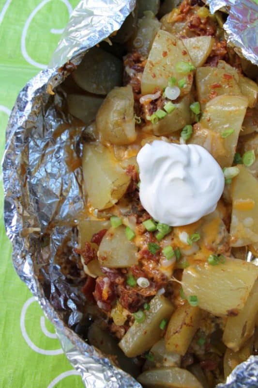 Potatoes being cooked in foil on a campfire with bacon, cheese, spring onions and sour cream. 
