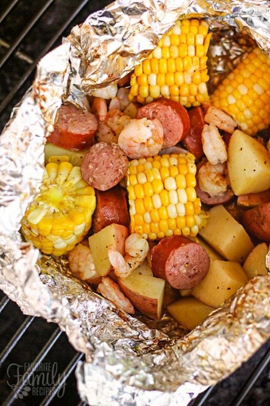 A foil dinner with corn, sausage, potatoes and shrimp being grilled on a campfire 