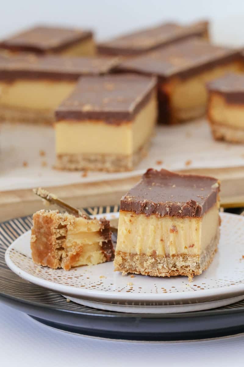 A piece of caramel slice with chocolate topping on a white plate.