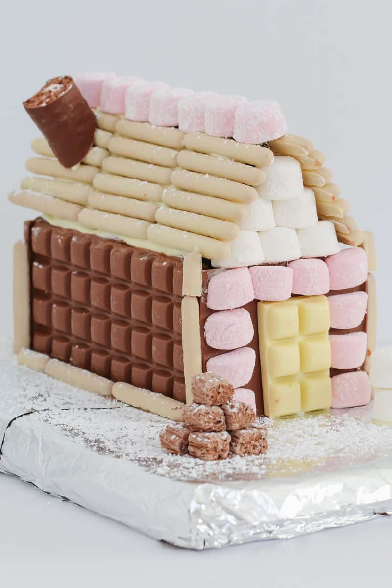 The front and side of a gingerbread house, decorated with chocolate bars, chocolate logs and marshmallows