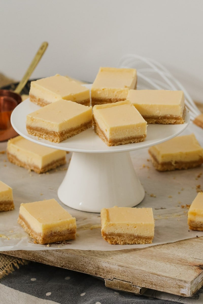 A white cake stand with squares of creamy lemon slice made with a biscuit crumb base