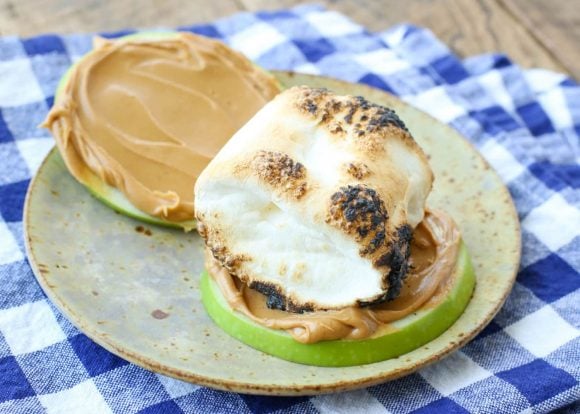 Slices of green apple with peanut butter and campfire toasted marshmallows. 