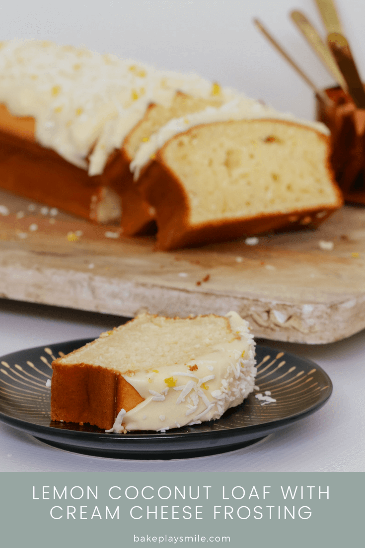 A slice of iced lemon loaf on a black plate in front of a wooden board with more slices