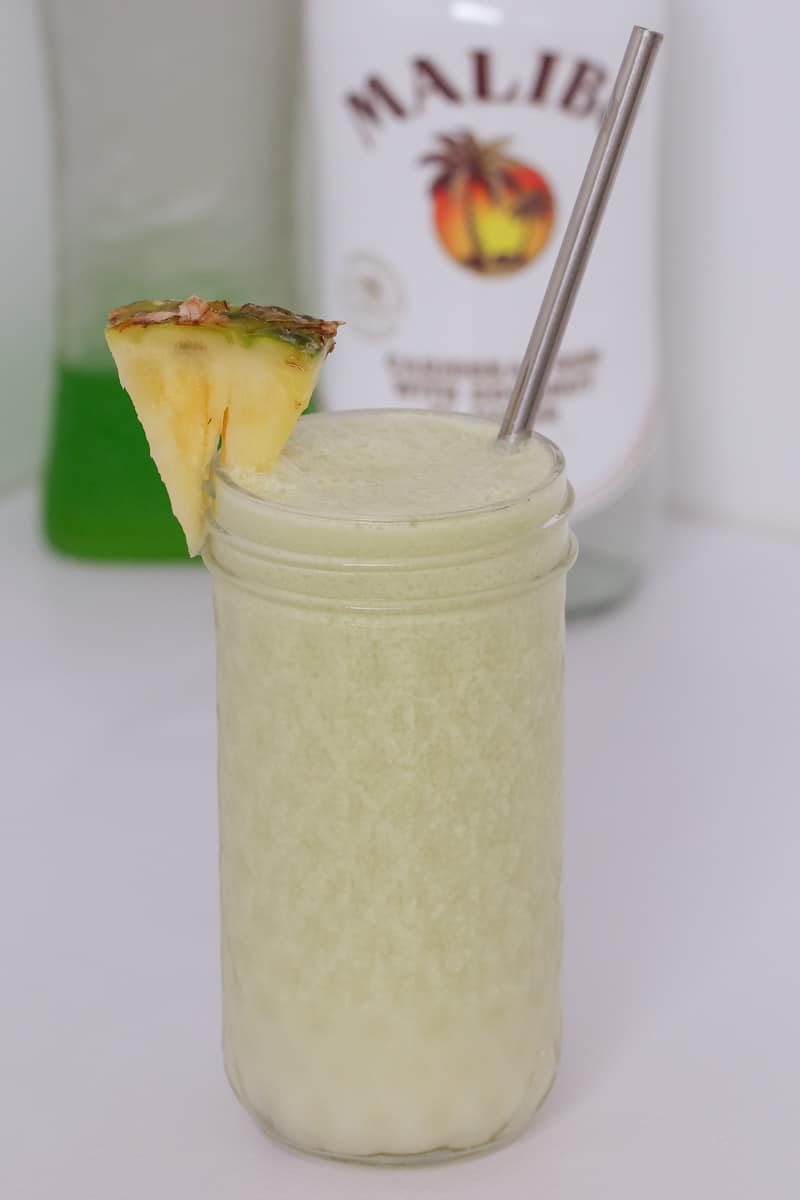 A textured glass jar filled with a creamy coloured cocktail, a pineapple wedges and a stainless straw
