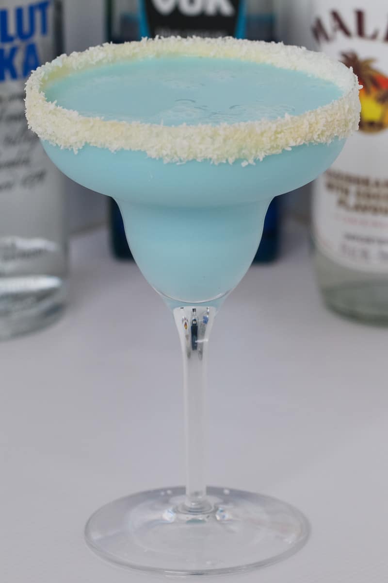 A close up of a blue cocktail in a sugar rimmed cocktail glass