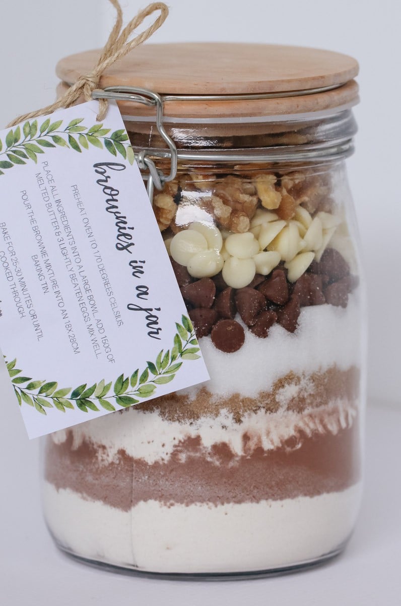 A glass lidded jar with a label attached, filled with dry ingredients to make cookies