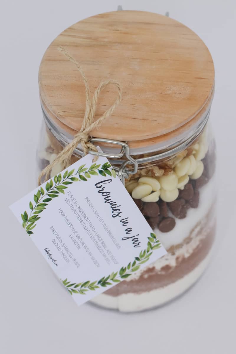 A glass jar with a label attached, filled with layers of ingredients to make cookies