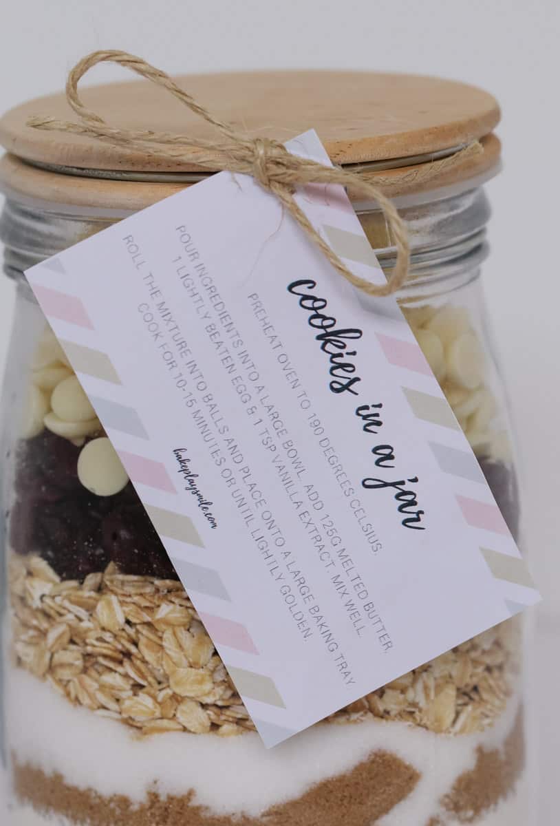 A close up of a label for \'Cookies in a Jar\', tied to a glass jar filled with layers of dry ingredients