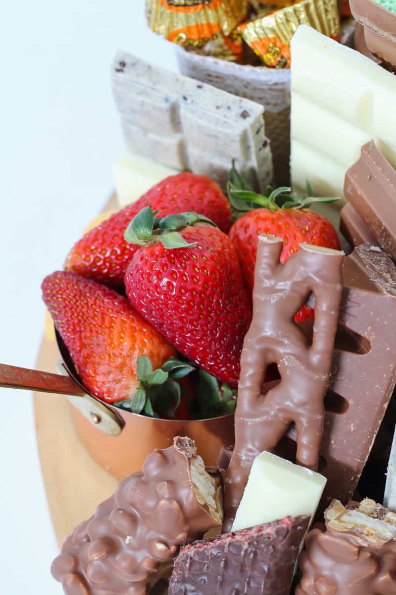 A copper measuring cup filled with fresh strawberries and surrounded with various chocolate treats