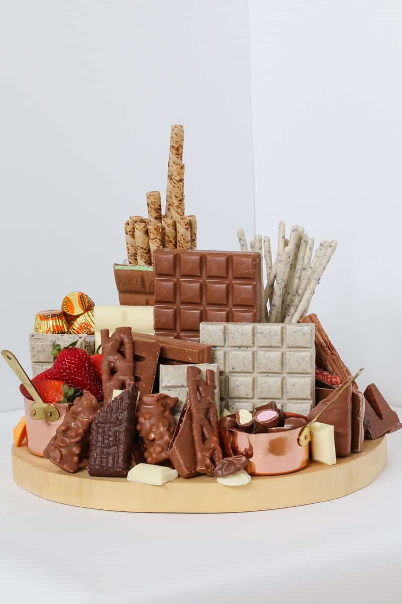 A selection of various chocolate bars and chocolate treats, with strawberries on a wooden platter