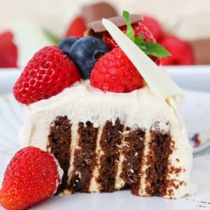A slice of a chocolate log layered with cream, covered with cream, berries and a white chocolate shard