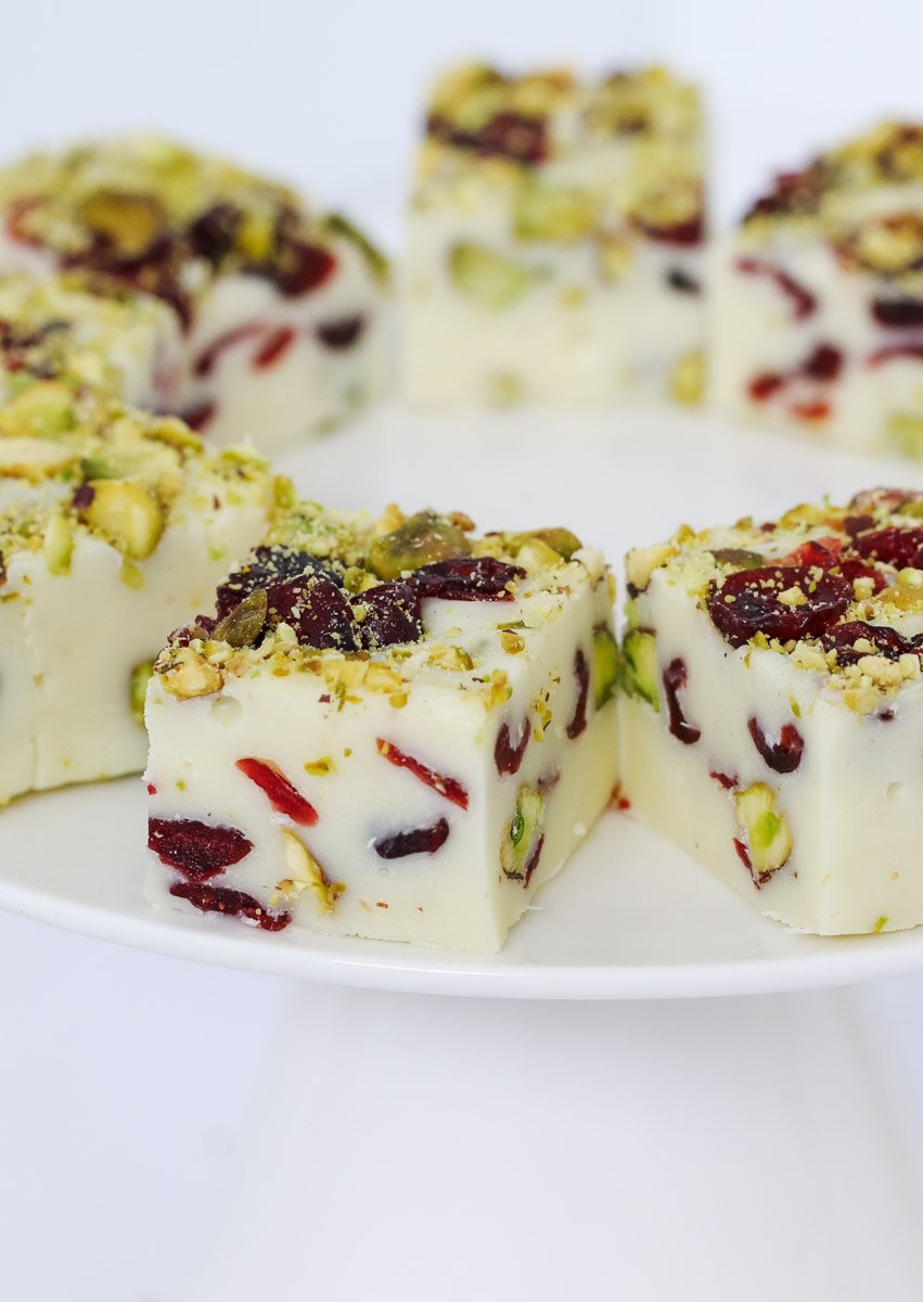 Pieces of a white chocolate fudge filled with cranberries and pistachio on a white plate