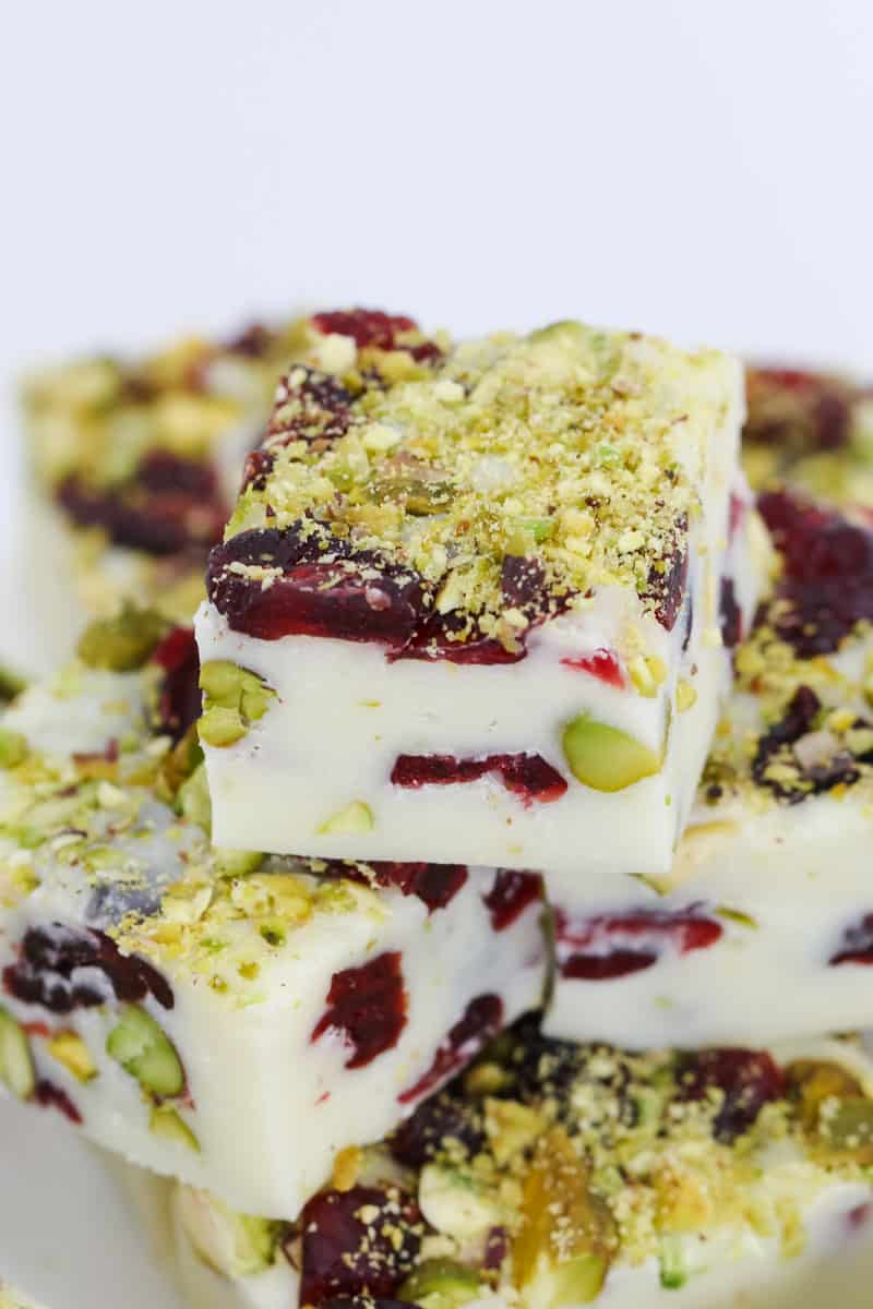 A close up of a stack of white chocolate fudge squares filled with cranberries and pistachios