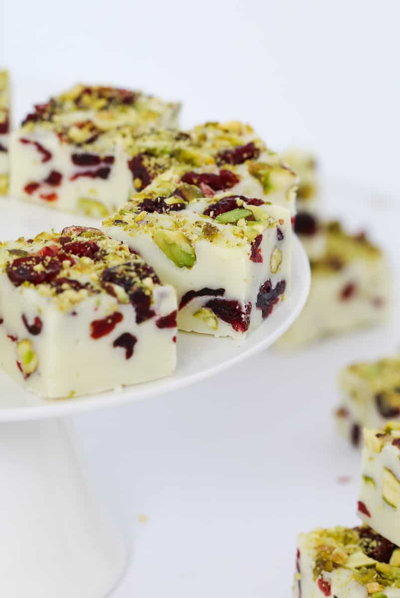 Pieces of a white chocolate fudge filled with cranberries and pistachios on a white cake plate