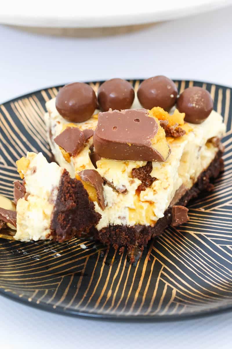 Chunks of chocolate honeycomb and malted milk balls decorating a half-eaten serve of creamy cheesecake.