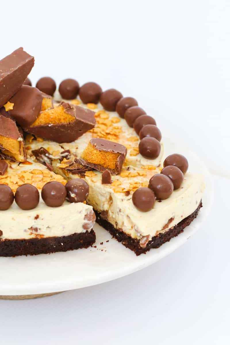 A slice of cheesecake topped with chocolate coated honeycomb and Maltesers being removed from the entire cheesecake.