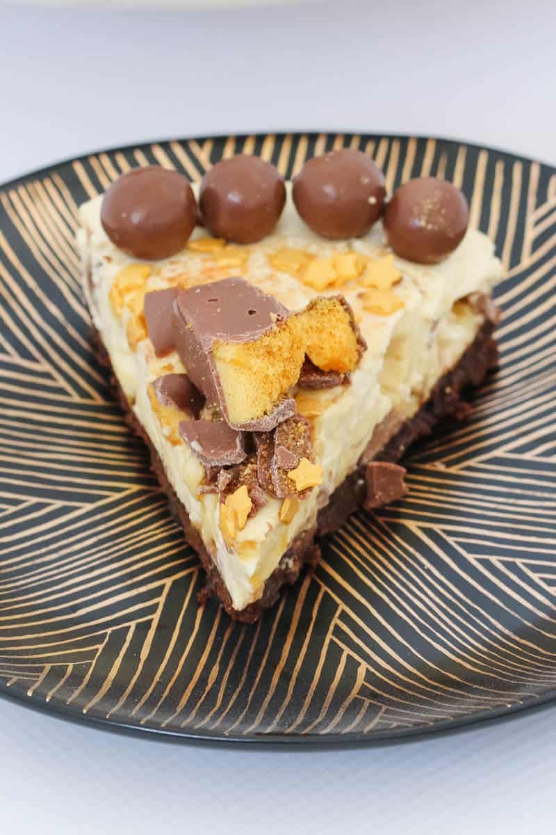 A slice of honeycomb and chocolate cheesecake on a black and gold plate. 