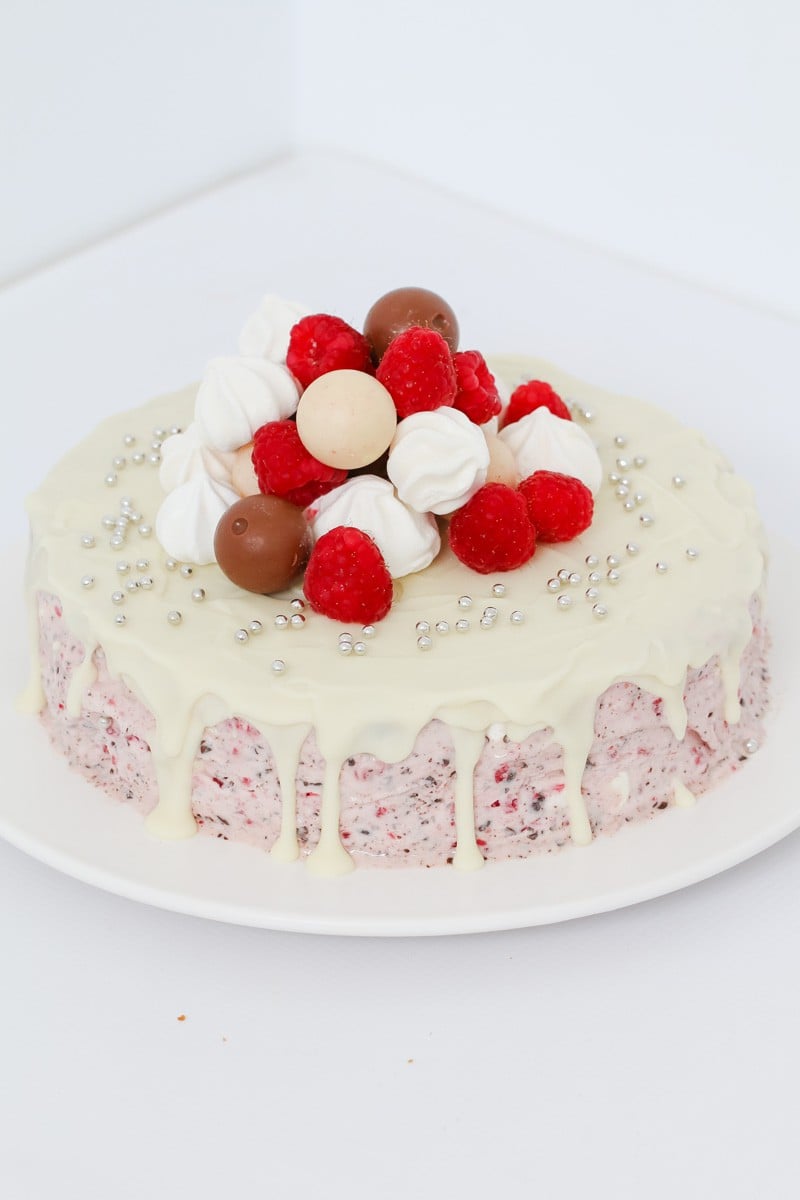 Raspberry ice-cream cake drizzed with white ice magic and a pile of raspberries, Lindt Balls and mini meringues on top
